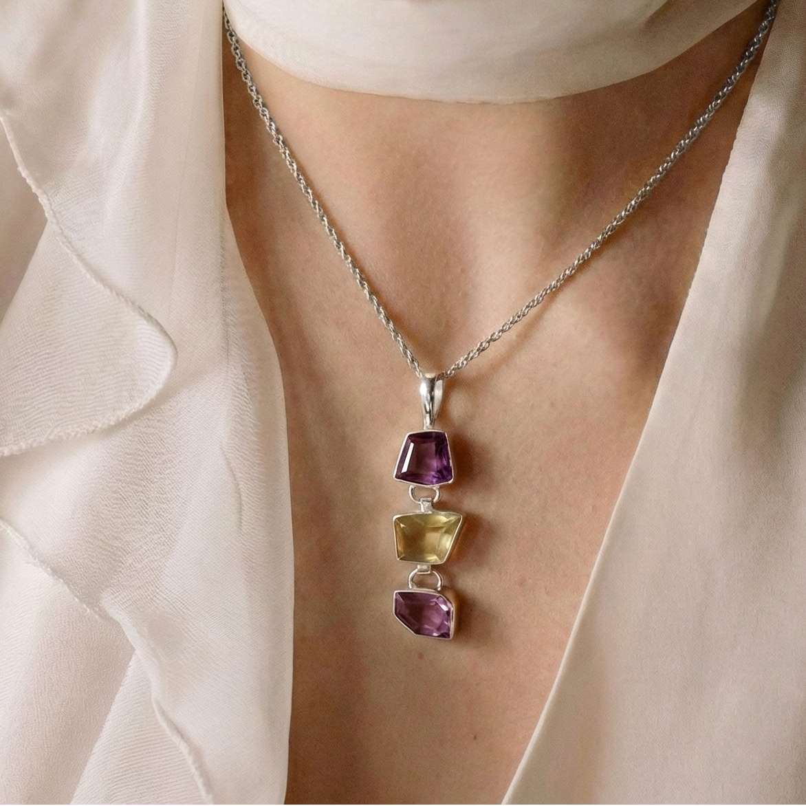 Close-up of a person wearing a necklace with multicolored gemstones, set against a neutral background.