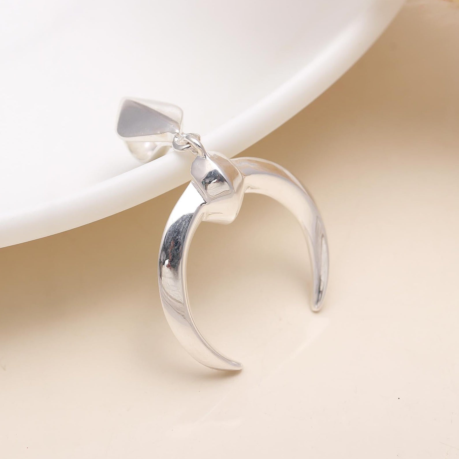 A crescent-shaped 925 sterling silver pendant on a delicate multilayered chain, placed near a white plate on a beige surface.