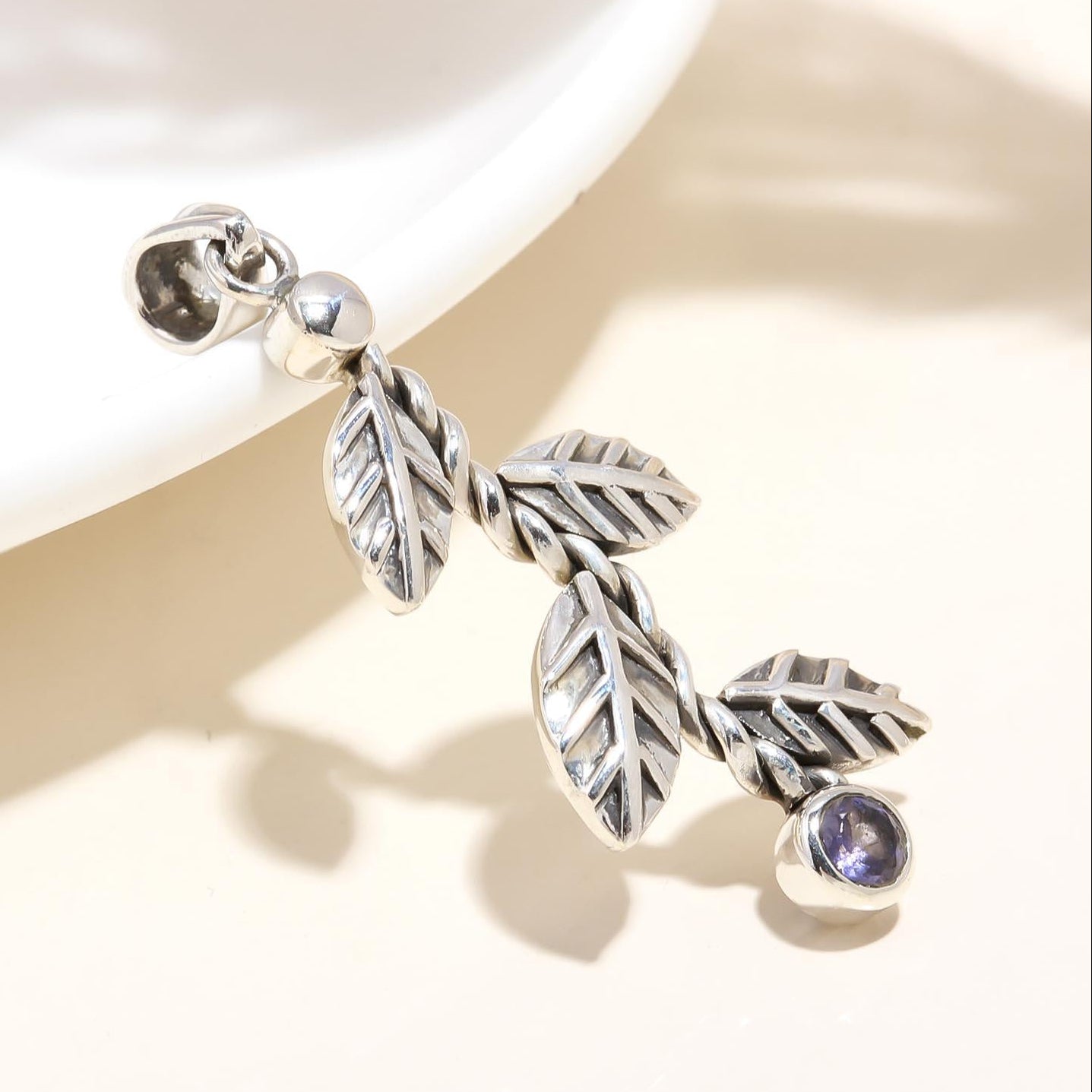 Silver leaf-shaped earring with a purple gemstone on a light background