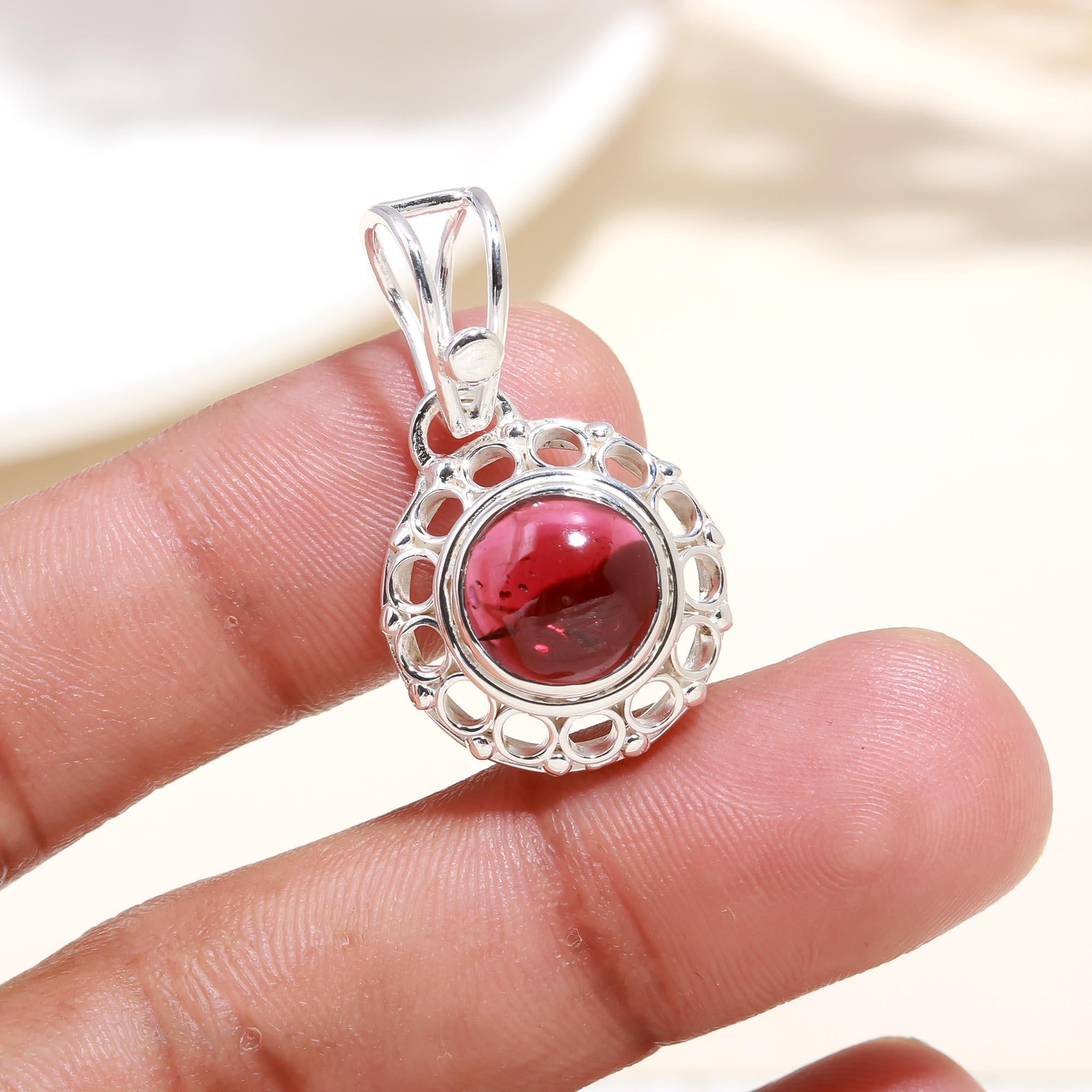 Silver pendant with a red gemstone held between fingers against a neutral background