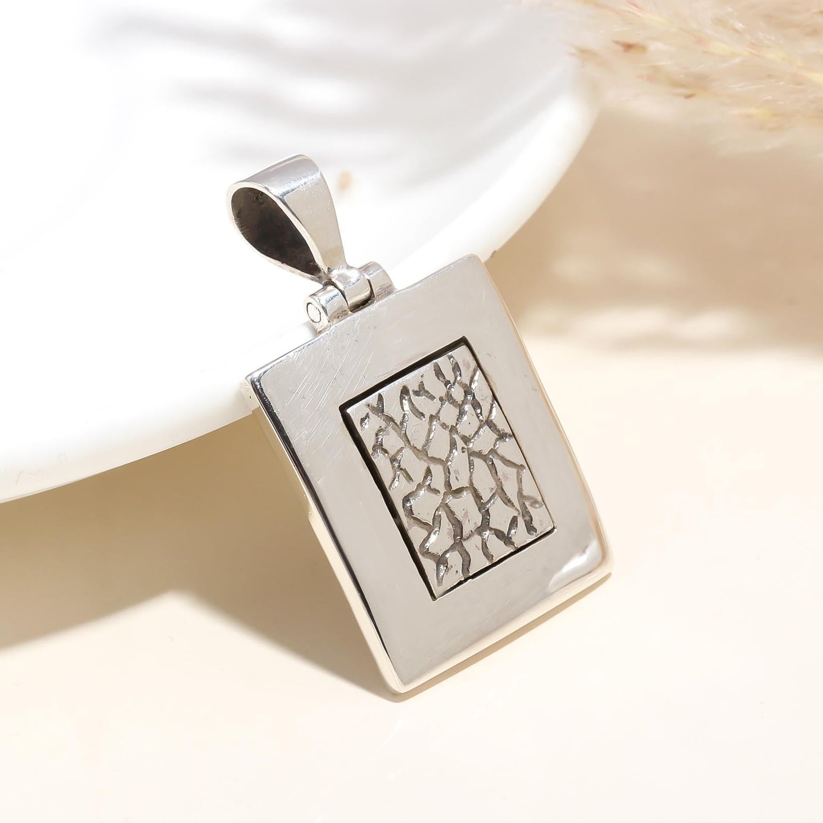 A high-quality 925 sterling silver square-shaped pendant with a geometric design, displayed on a white plate with a blurred background.