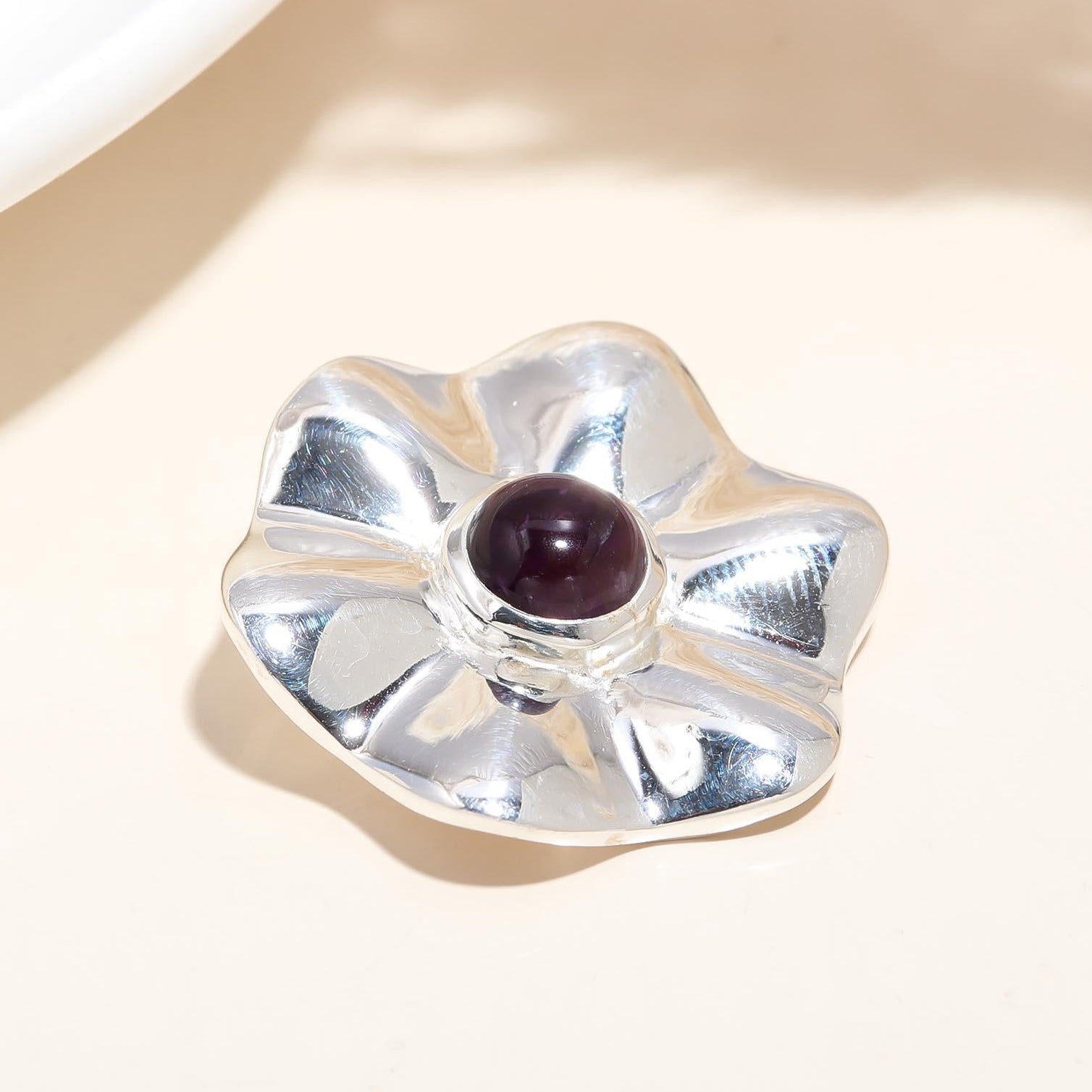 A sterling silver floral-shaped statement pendant with a central black gemstone, placed on a light-colored surface.