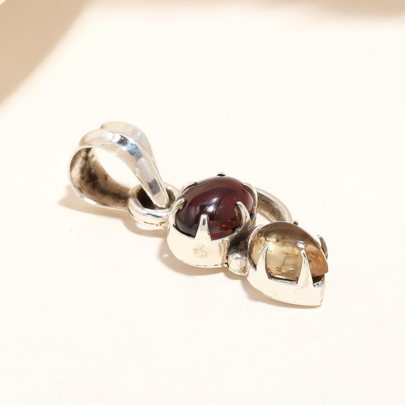 A sterling silver pendant featuring a natural garnet centerpiece surrounded by a metallic border on a light-colored surface.