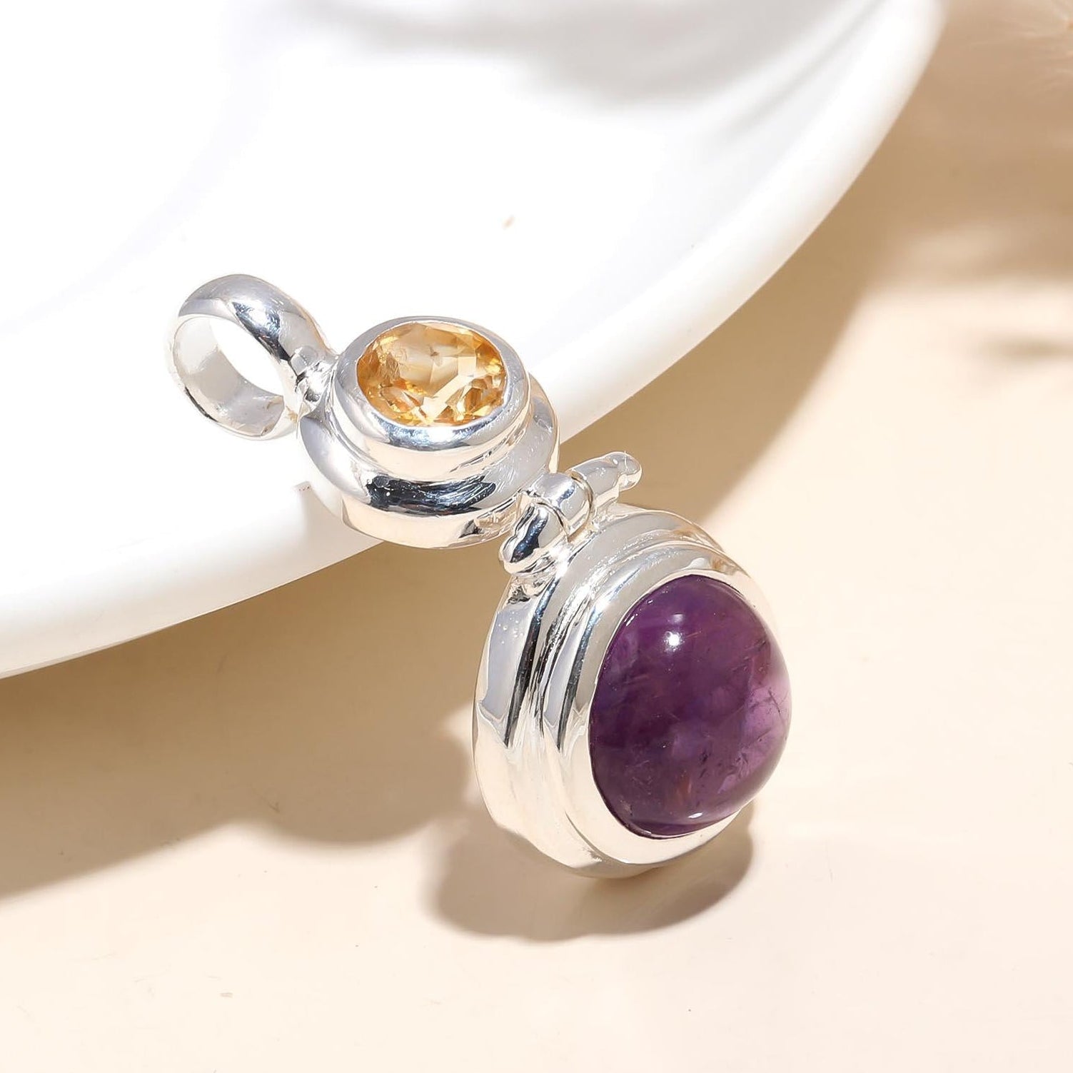 A sterling silver wholesale pendant featuring a large purple amethyst and a smaller citrine gemstone, attached to a silver pearl-like bead.