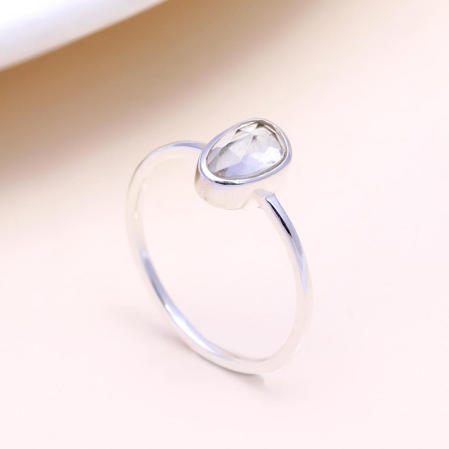 Silver ring with a clear gemstone on a beige background