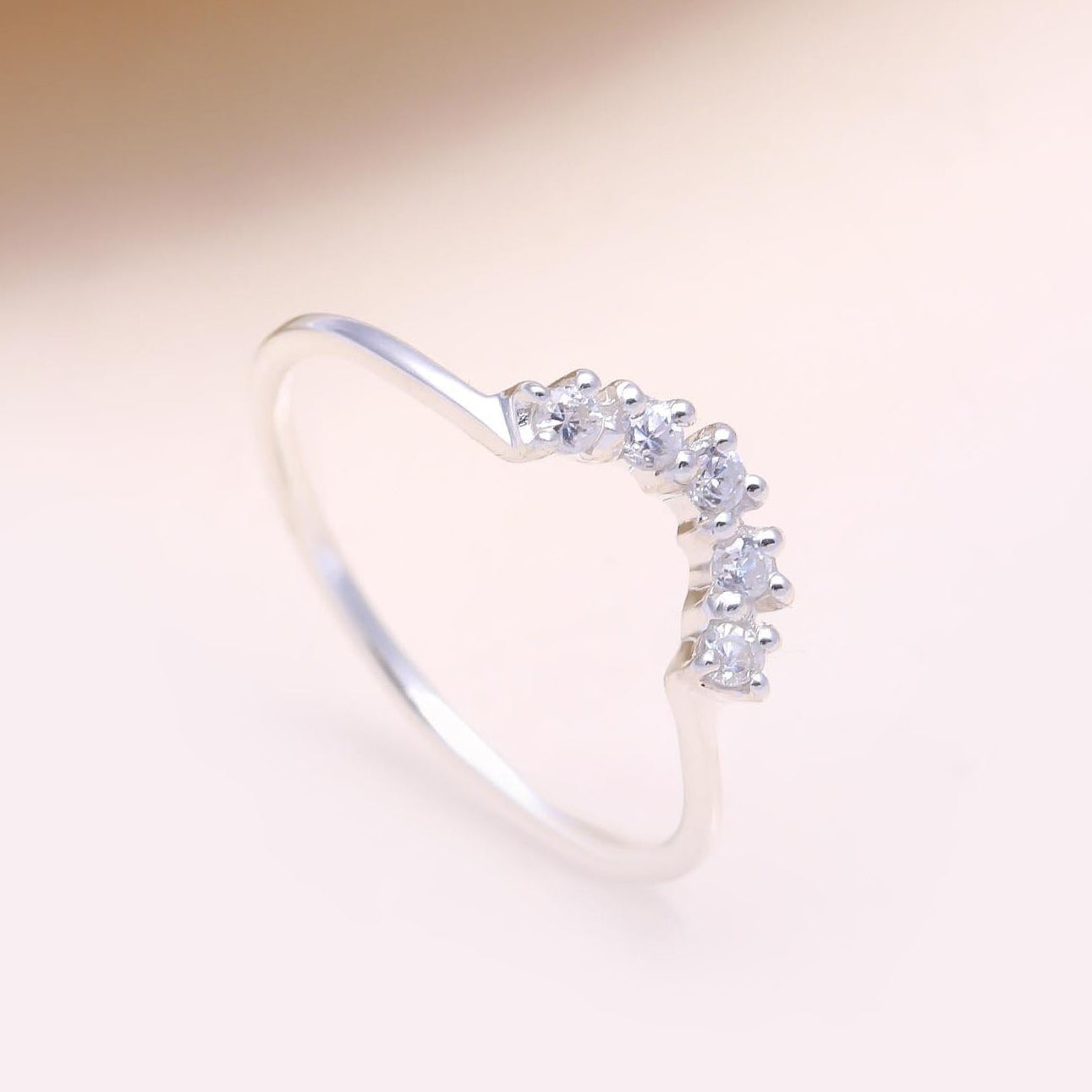 Silver ring with small diamonds on a light pink background