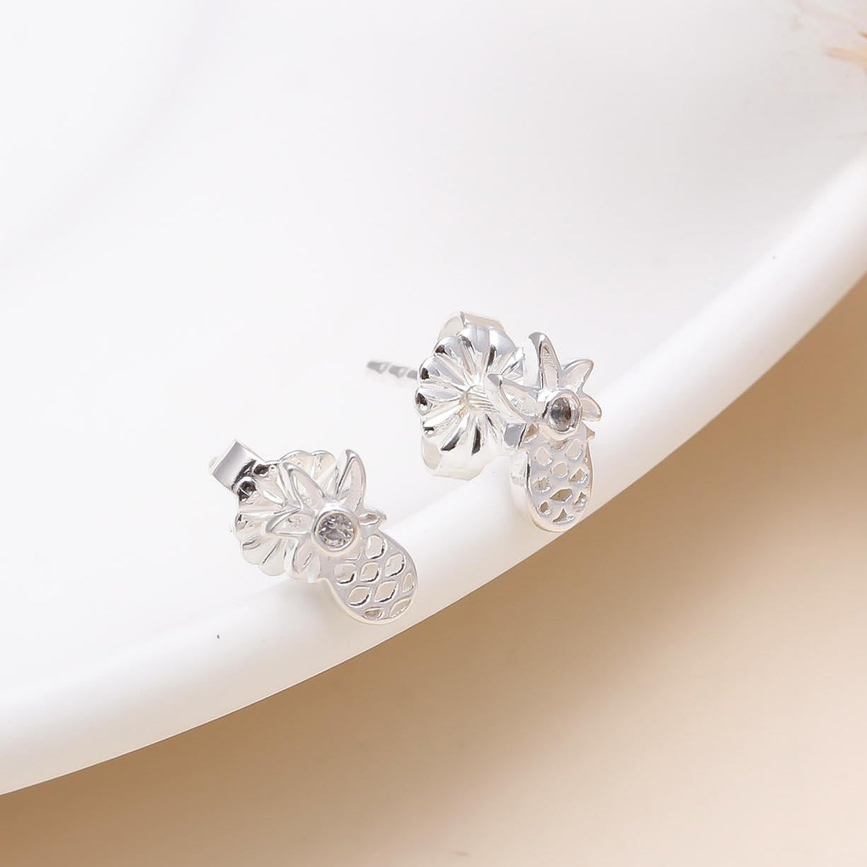 A pair of 925 sterling silver tropical pineapple stud earrings displayed on a white plate, featuring a cute and stylish pineapple shape with a polished finish.