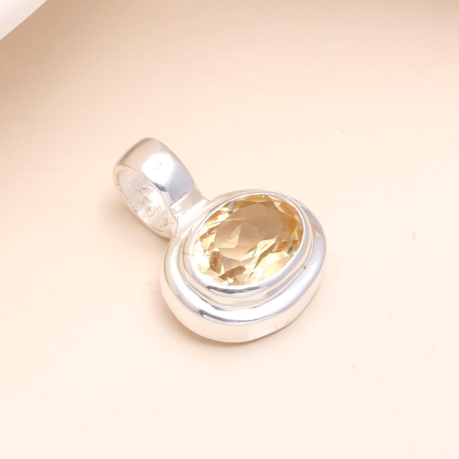 Silver pendant with a yellow gemstone on a beige background