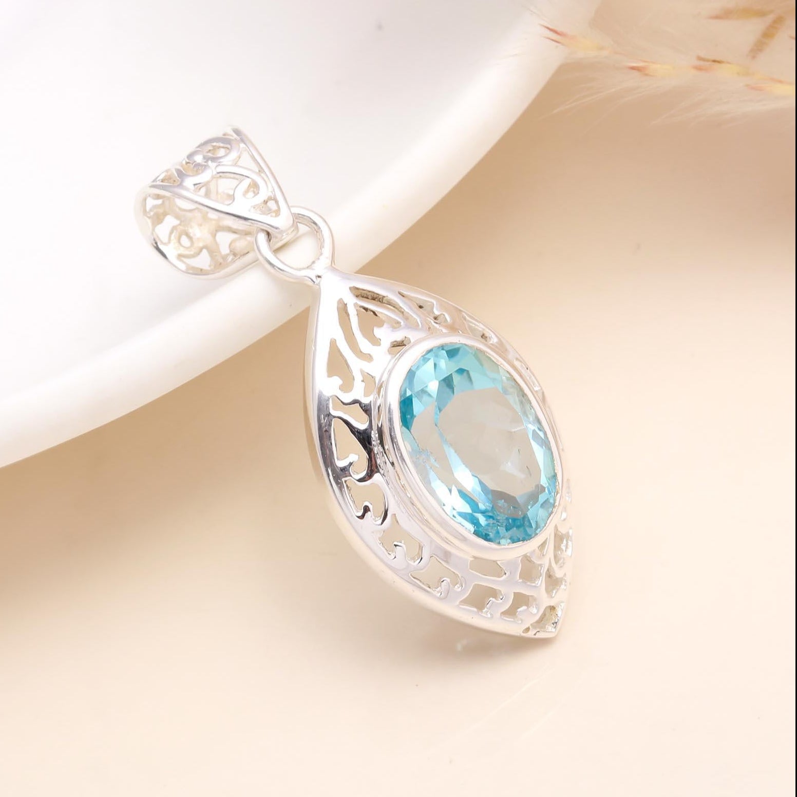 A 925 Sterling Silver Blue Topaz Filigree Pendant placed on a white surface, showcasing the pendant's intricate silver design and the blue topaz gemstone.