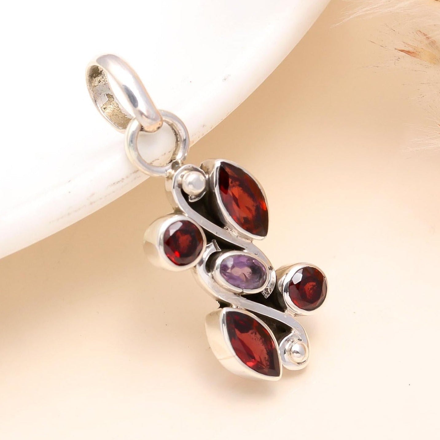 Silver pendant with red and purple gemstones on a light background