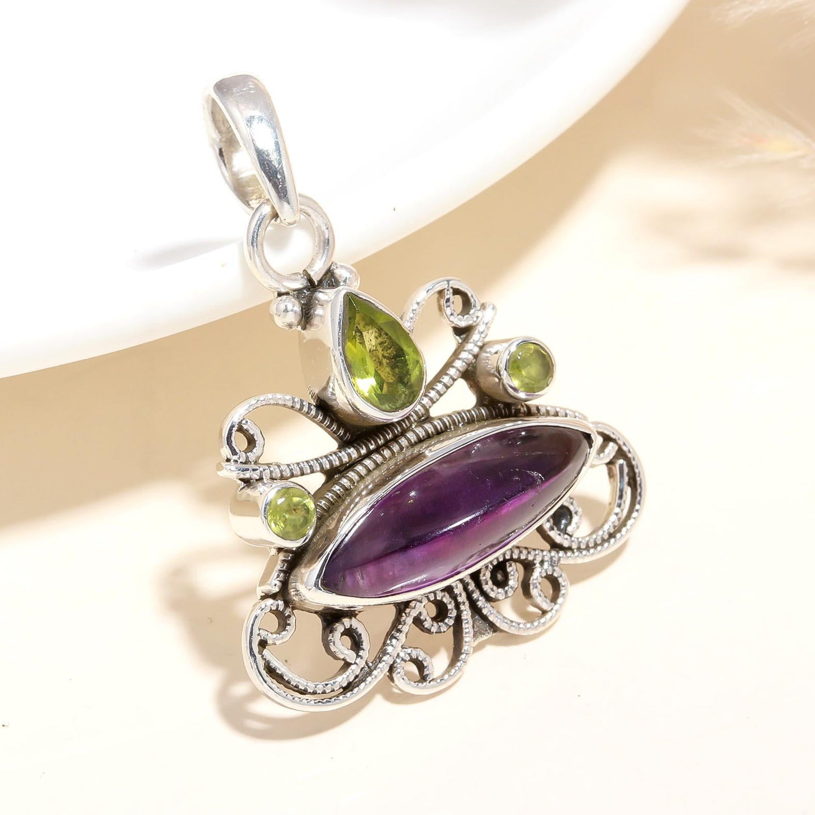A sterling silver pendant featuring a marquise-shaped amethyst with smaller peridot stones set in a filigree design.