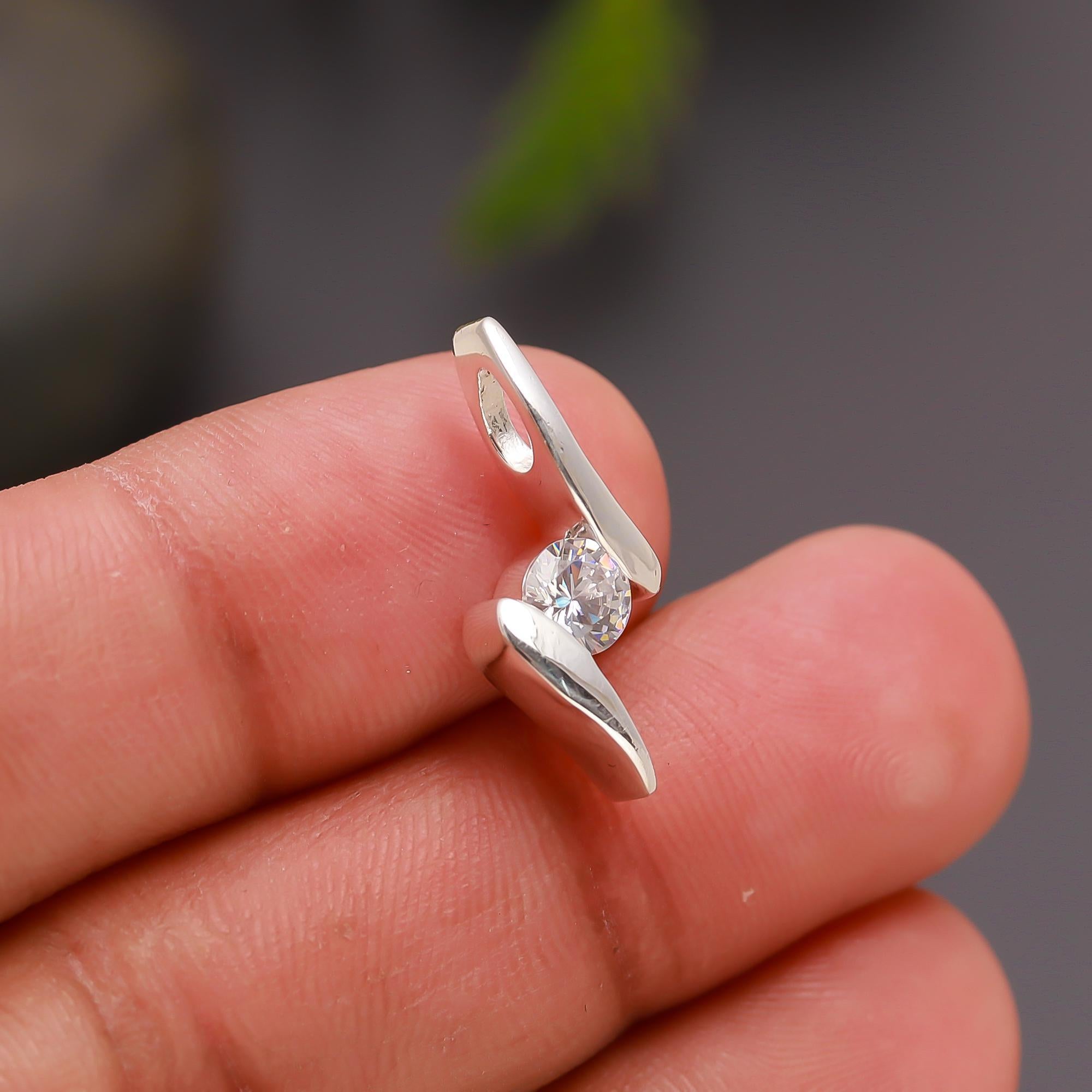 Silver ring with a diamond held between fingers against a blurred background