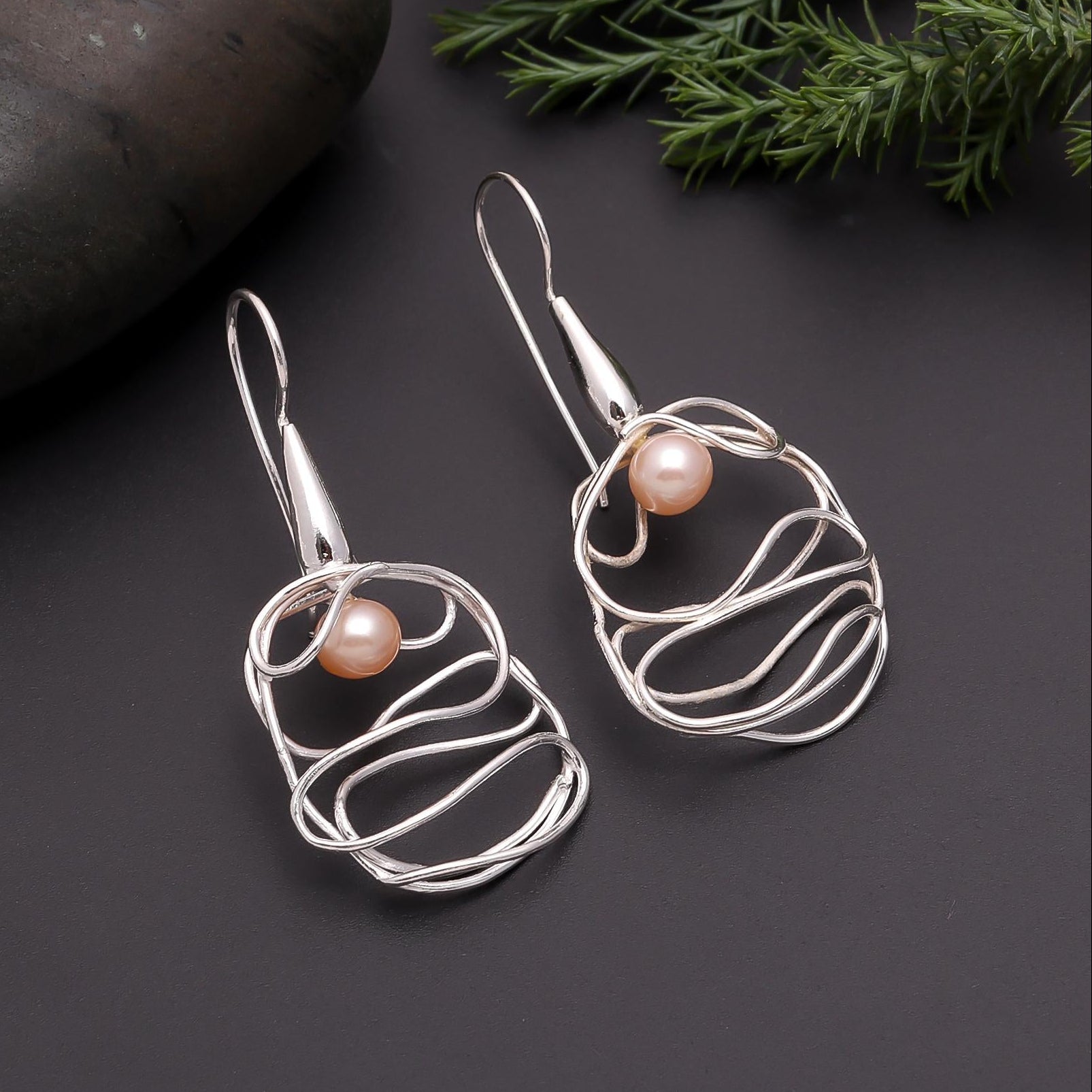 Silver wire earrings with pearls on a dark surface with greenery