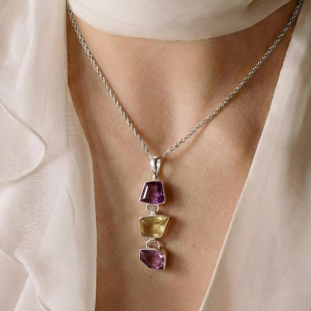 Close-up of a person wearing a necklace with multicolored gemstones, set against a neutral background.