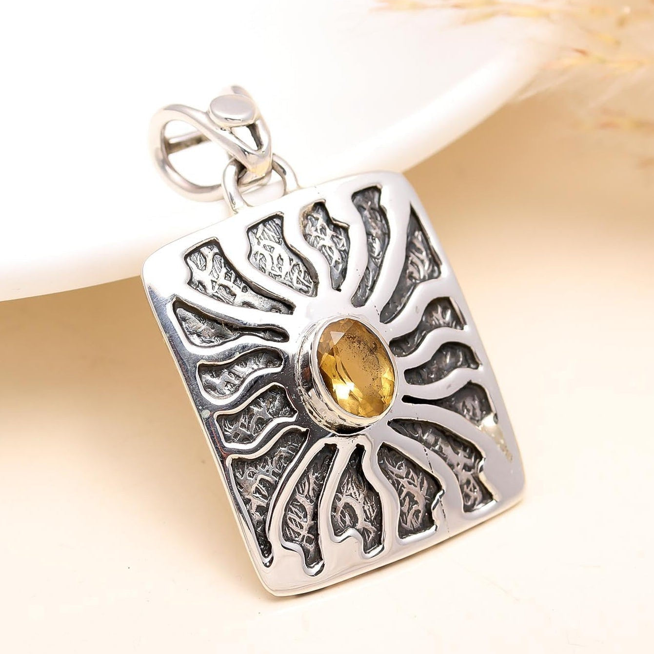 Silver pendant with intricate design and a yellow gemstone on a light background