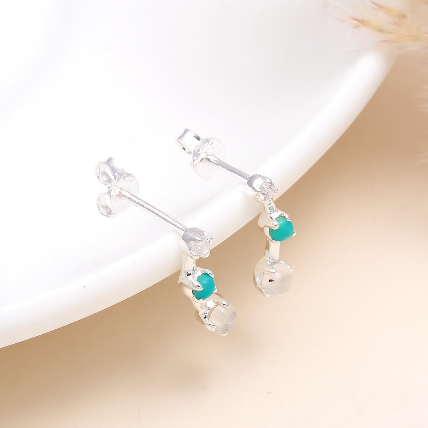 A pair of 925 sterling silver stud earrings with turquoise and clear quartz stones, displayed on a white surface.