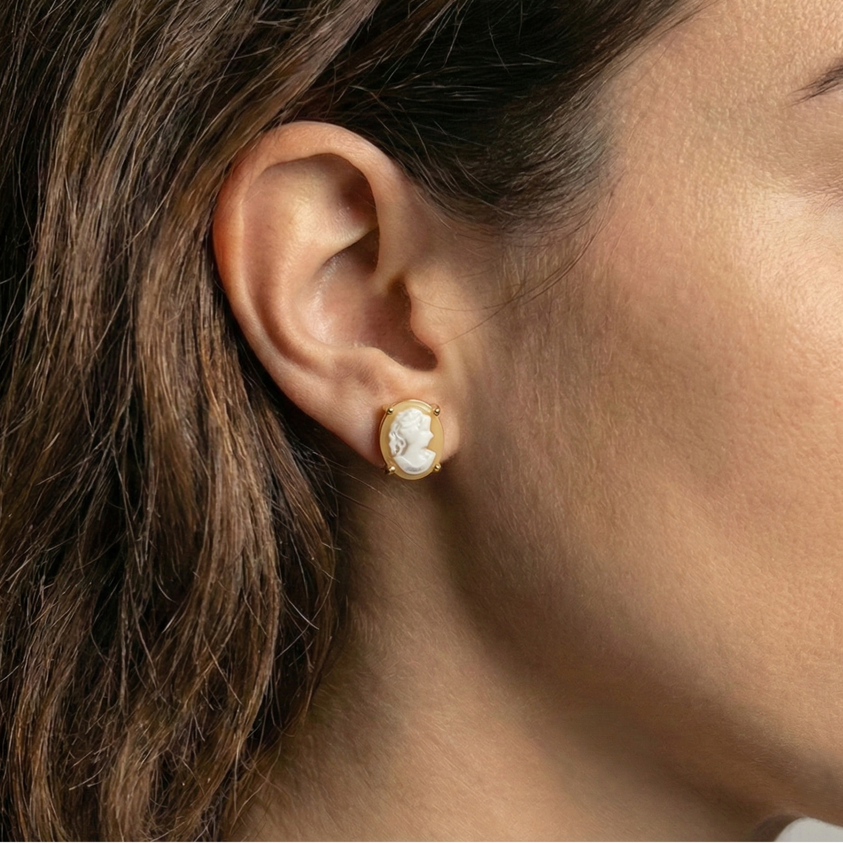 Close-up of an ear wearing a gold earring with vintage cameo studs