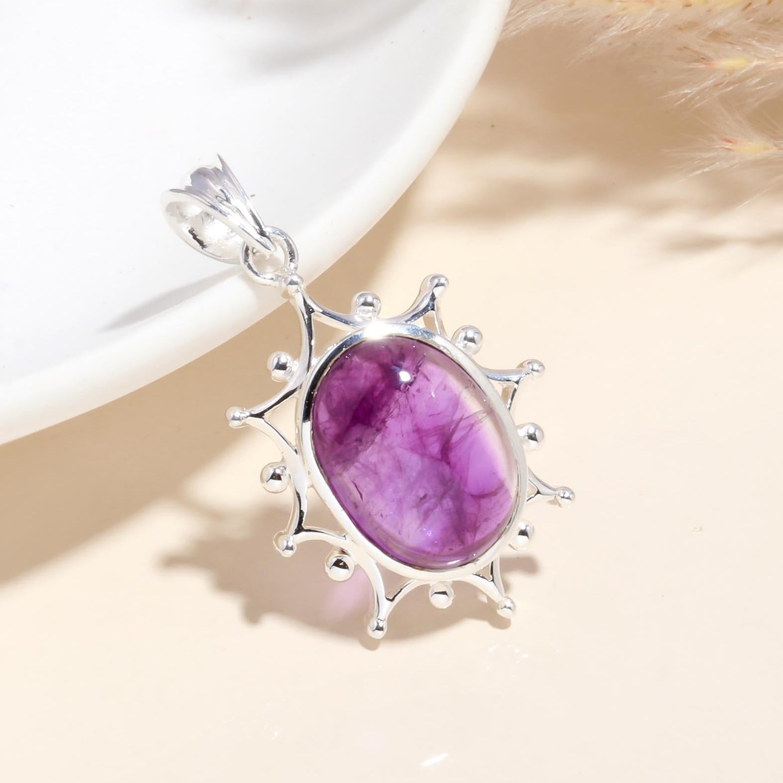 A sterling silver pendant with a natural amethyst gemstone set in a sunburst design, displayed against a neutral background.