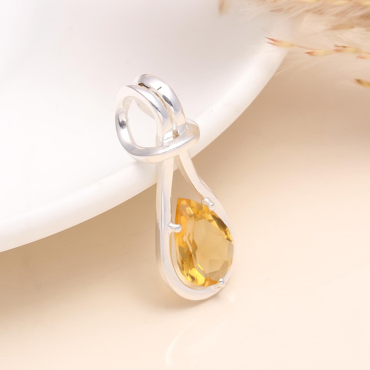 A 925 Sterling Silver Modern Teardrop Citrine Pendant placed on a white surface, showcasing the pendant's sleek and contemporary design with a teardrop-shaped citrine gemstone.