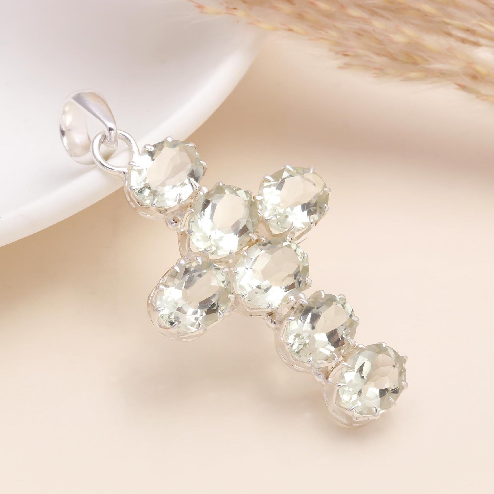 Silver cross pendant with clear gemstones on a soft beige background