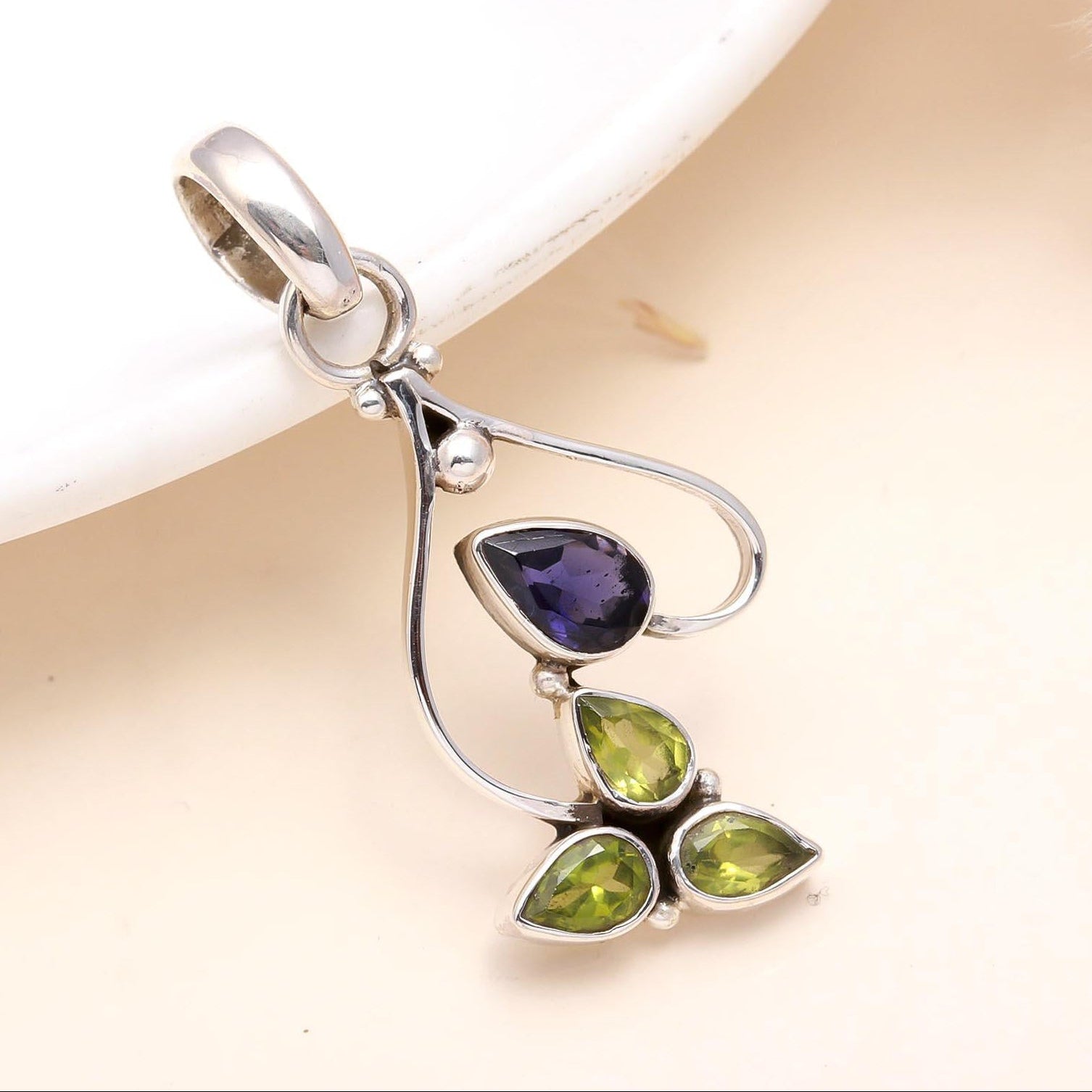 Silver pendant with purple and green gemstones on a beige background
