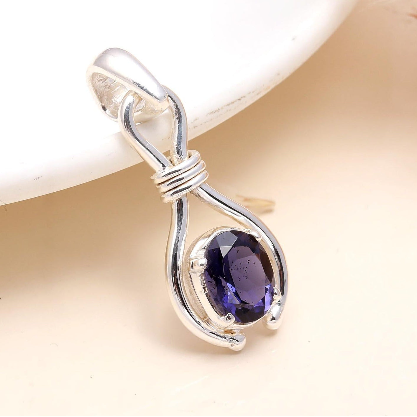 A 925 Sterling Silver Blue Faceted Iolite Pendant placed on a white surface, highlighting the gemstone's facades and the silver mounting.