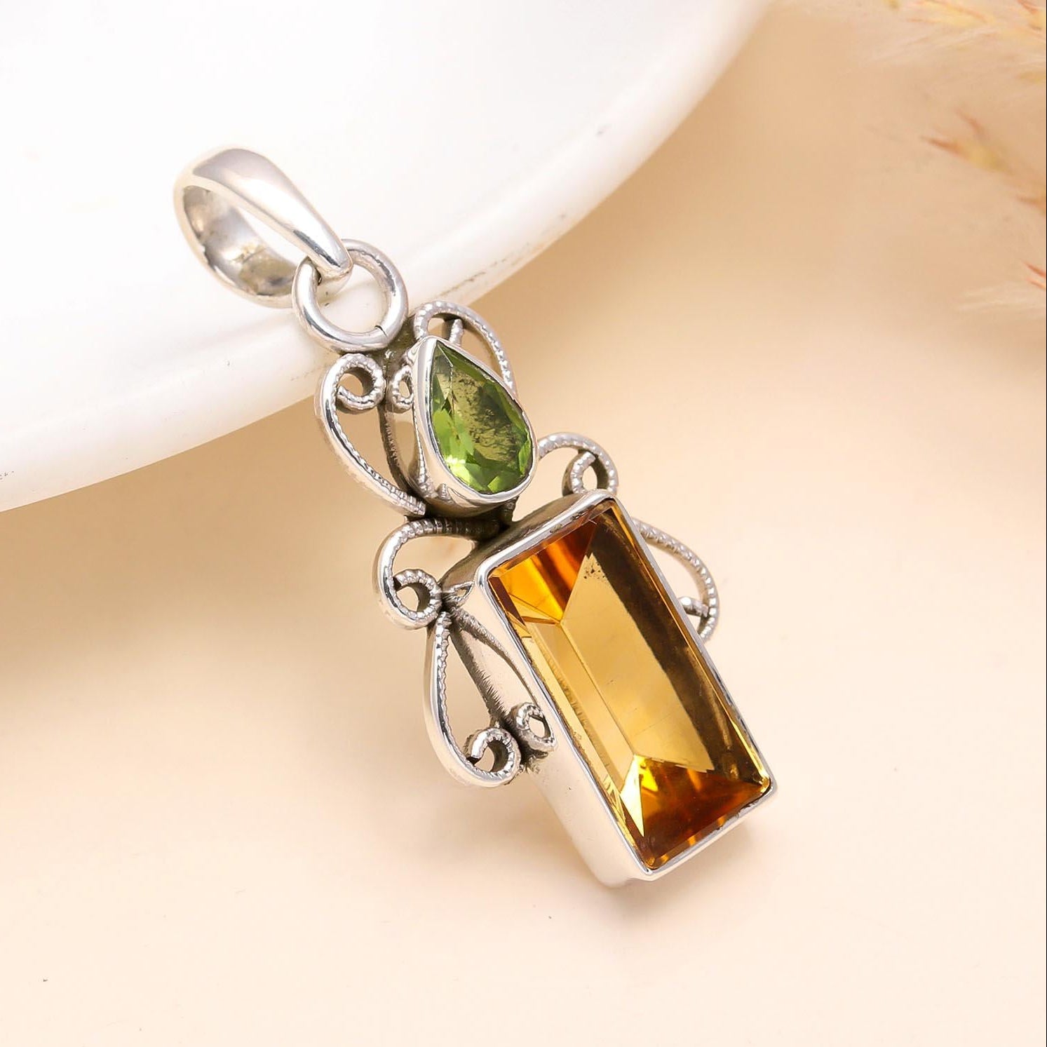 A sterling silver pendant featuring a rectangular citrine gemstone and a round peridot gemstone, arranged in a filigree design.
