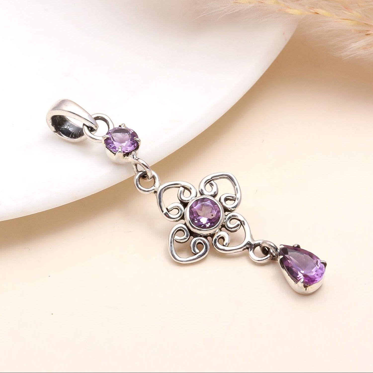 A sterling silver pendant with a deep purple amethyst gemstone and intricate filigree detailing, presented on a white surface.