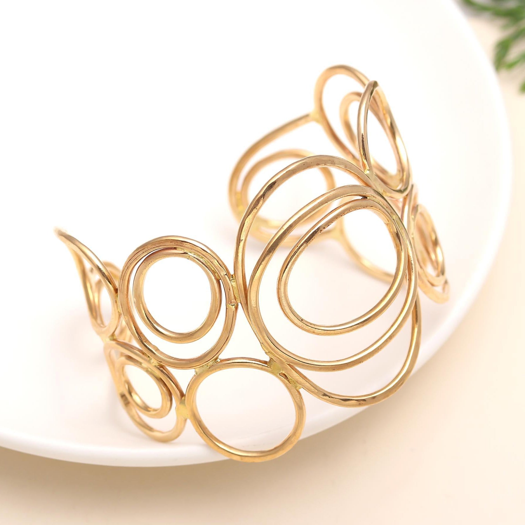 Gold spiral cuff bracelet on a white plate with a beige background