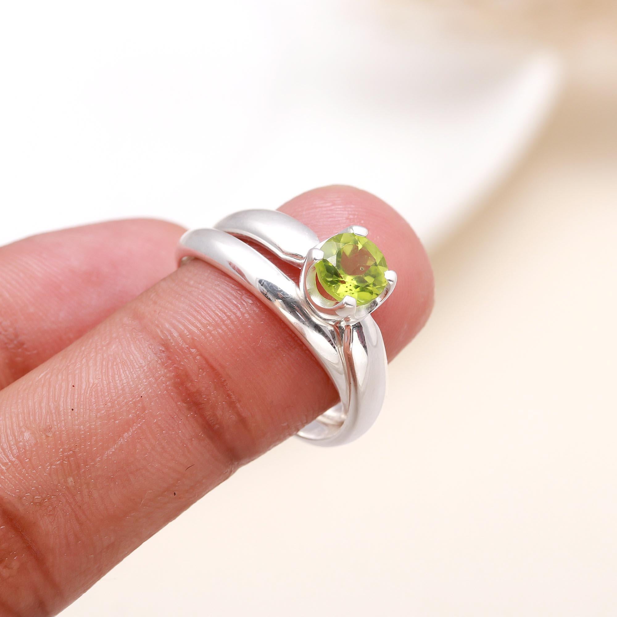 Silver ring with a green gemstone on a finger against a neutral background