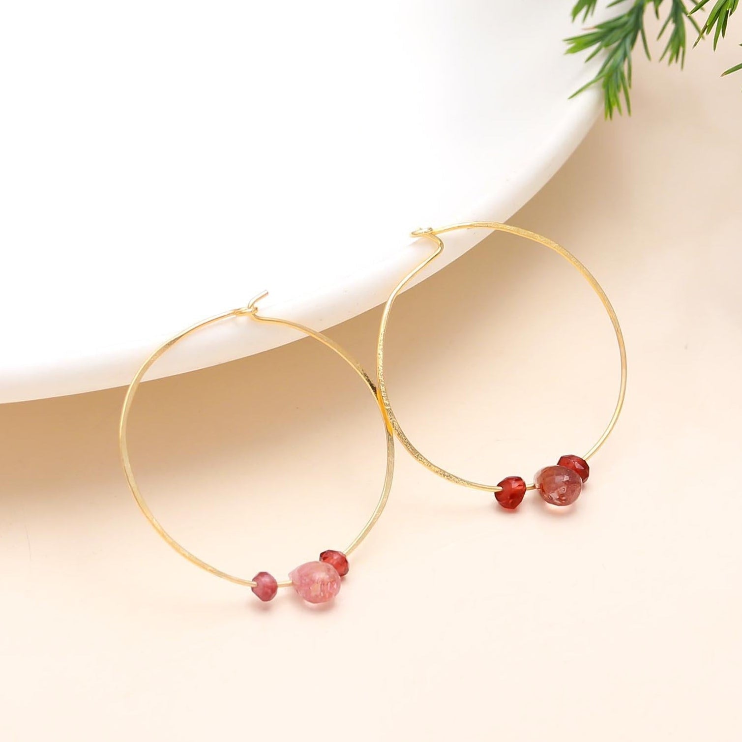 Gold hoop earrings with red beads on a beige background